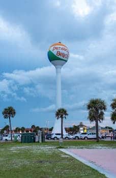 Scenic view of the iconic Pensacola Beach water tower with palm trees and cloudy sky.